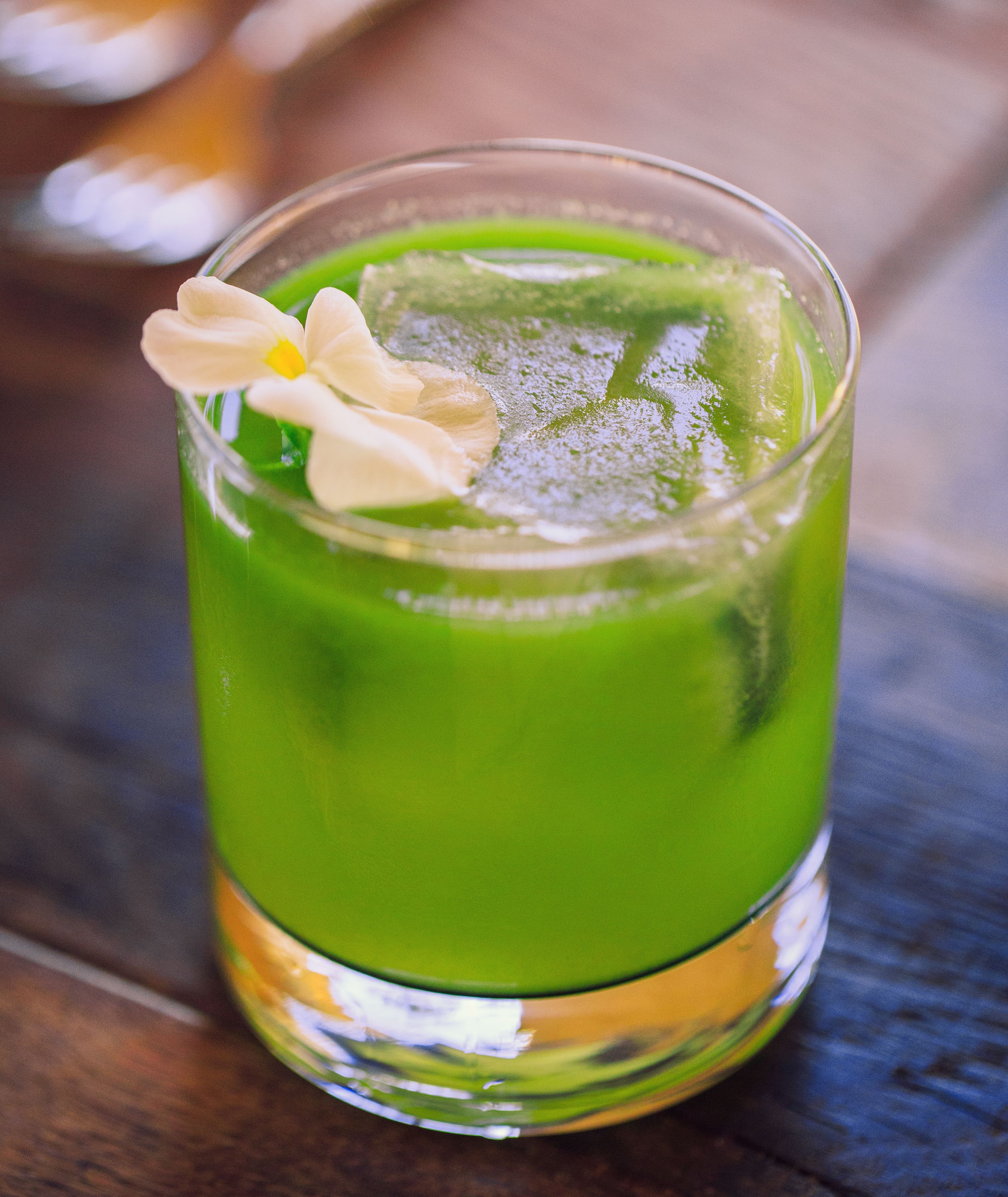 Un vaso de bebida verde con una decoración floral sobre una superficie de madera.