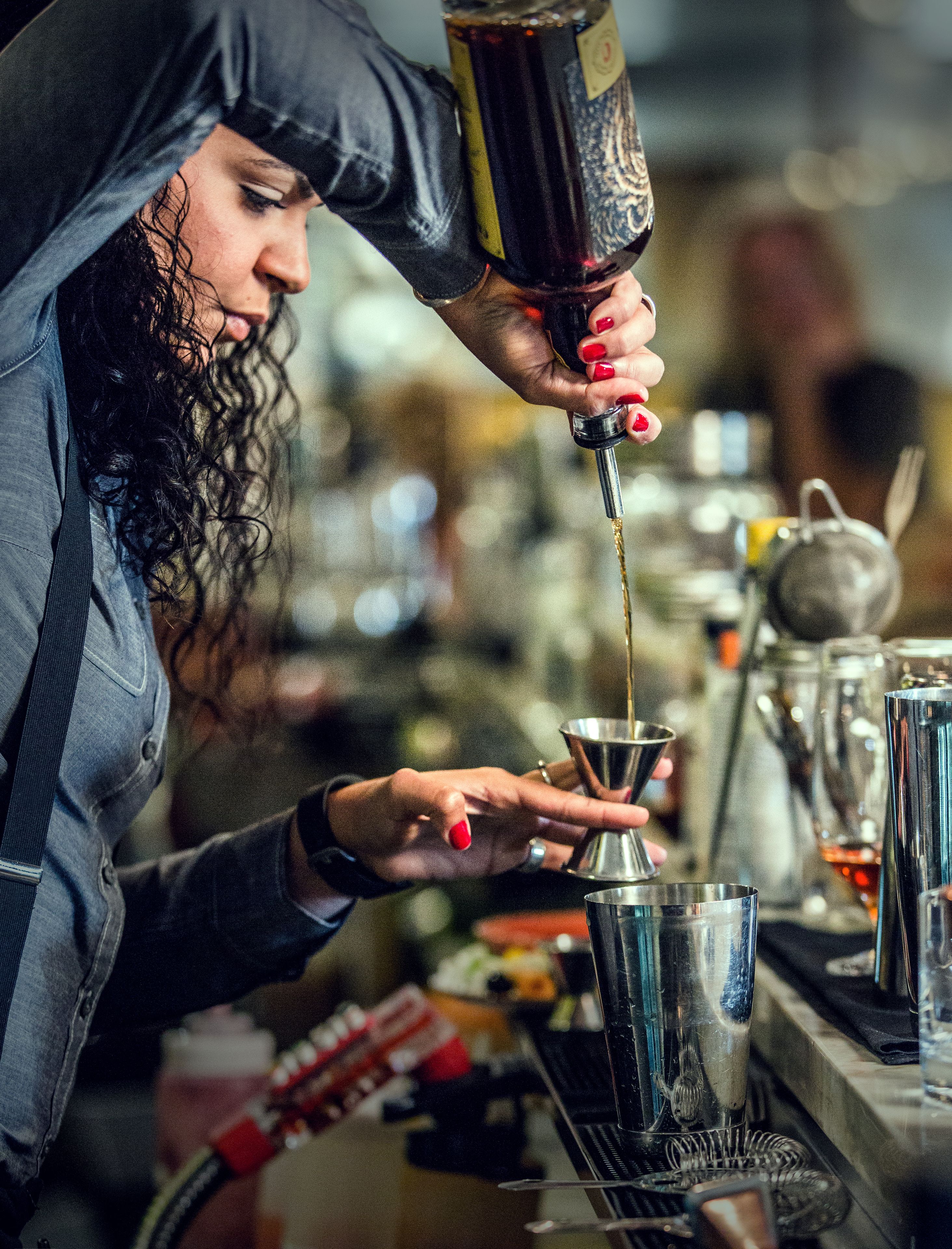A bartender pouring a drink into a shaker.