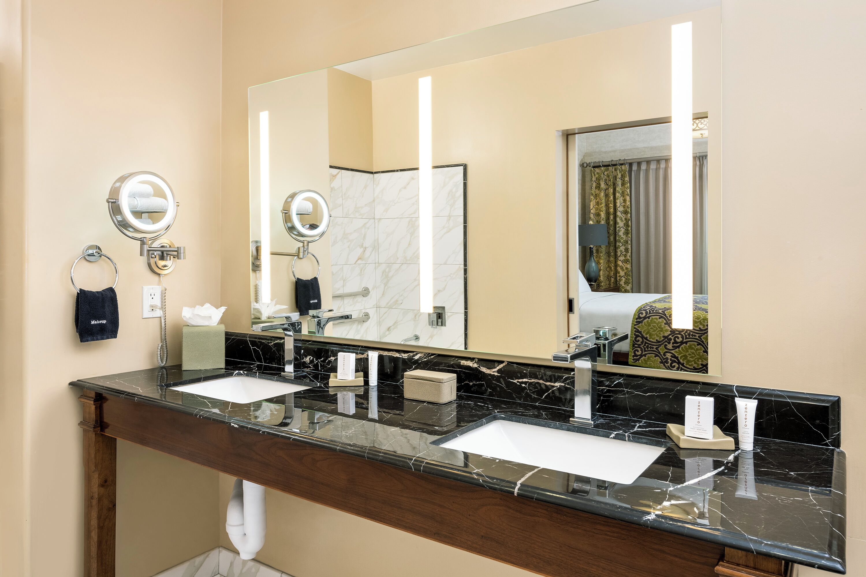 A hotel bathroom with two sinks, a large mirror, and a towel rack.