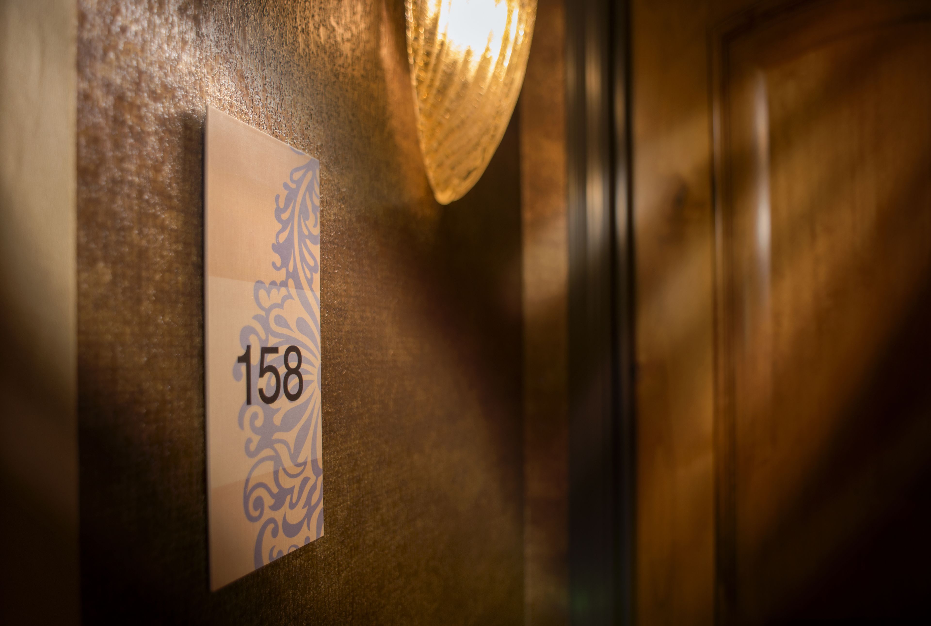 A close-up of a room number sign, 158, on a textured wall with a decorative pattern.