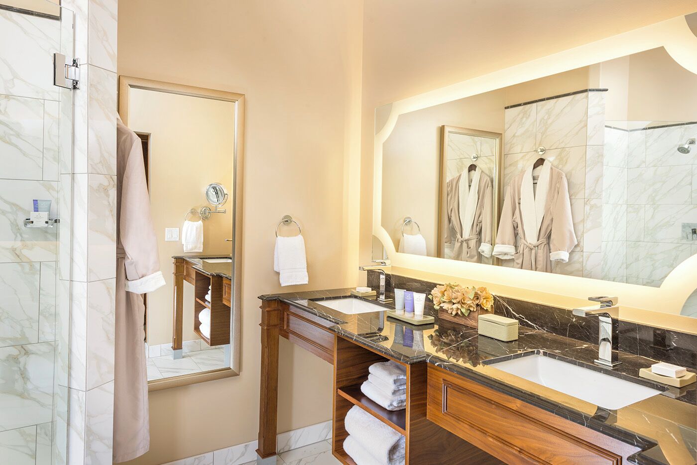 Un baño moderno con un espejo grande, dos lavamanos, una ducha y un tocador con encimera de mármol.