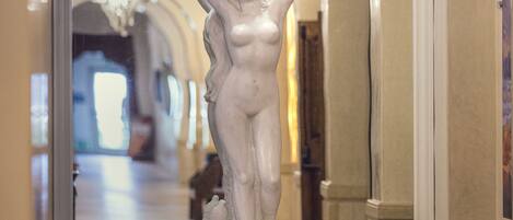 Una estatua de mármol en un pasillo con arcos y candelabros.
