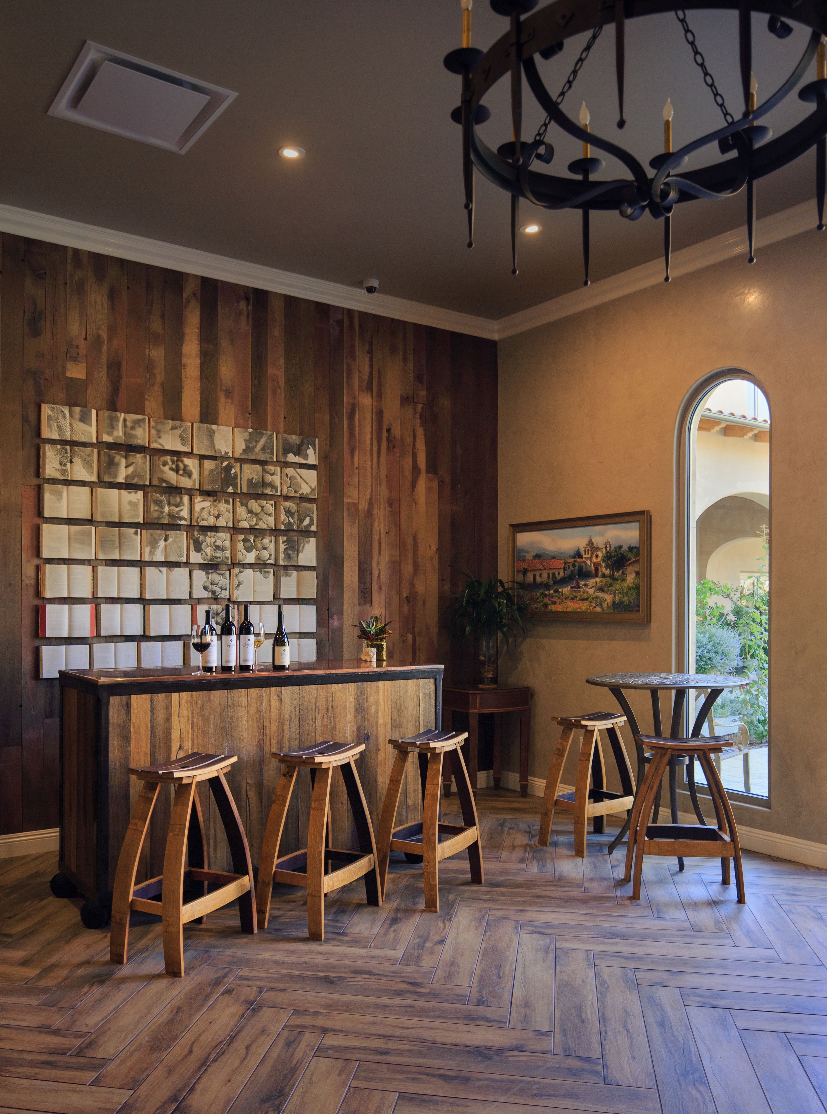 A bar area with wooden bar stools, a wine display, and a large wooden wall with artwork.
