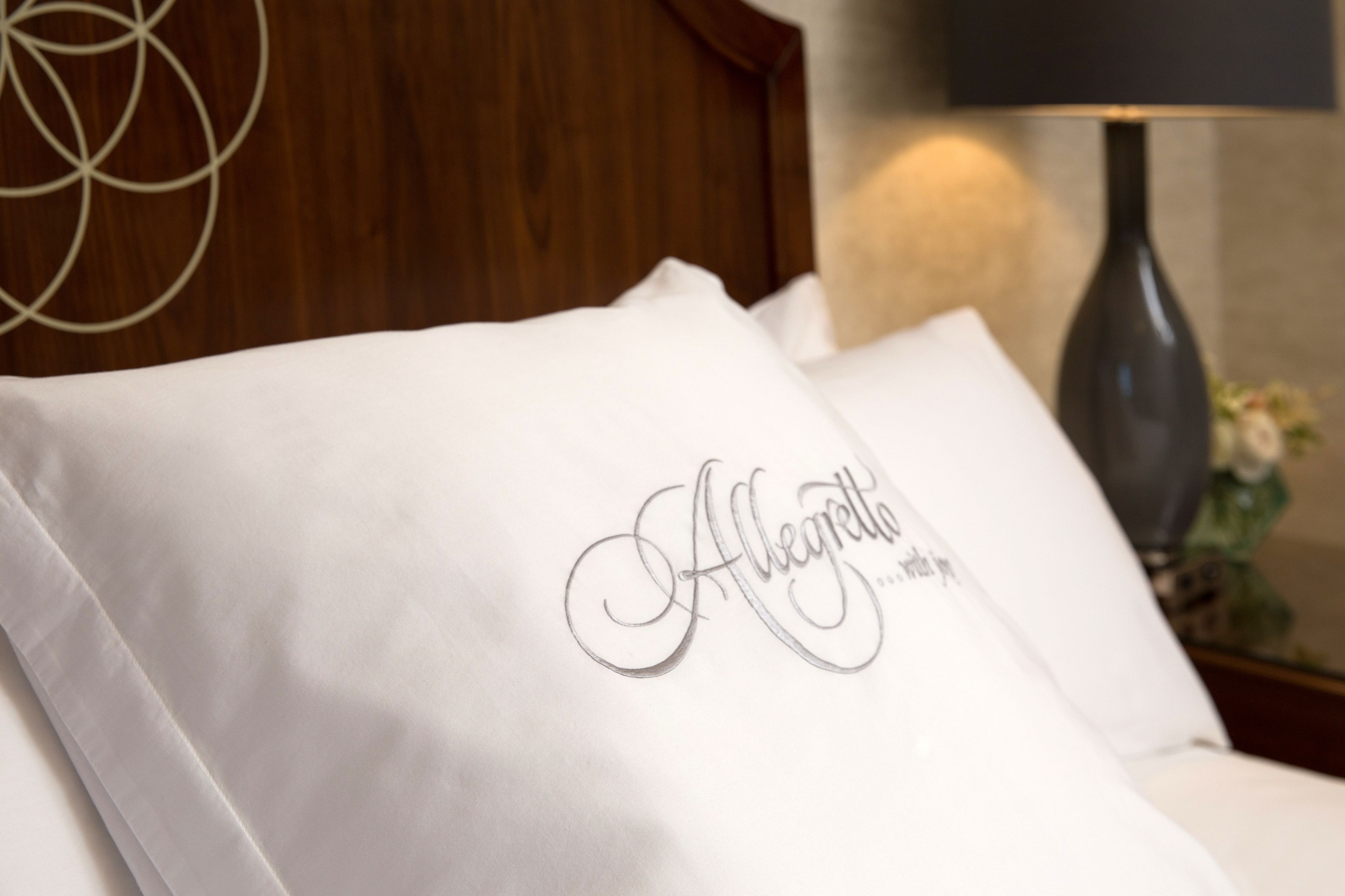 Een net opgemaakt bed met een kussen waarop de naam 'Alegrete' in sierletters geborduurd staat.