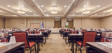 Un salón de banquetes con filas de mesas, cada una con copas de vino y sillas rojas.