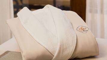 A neatly folded beige towel with a spa logo on a textured surface, likely a bed or a seating area, with a view of a dining table and chairs through a glass partition.