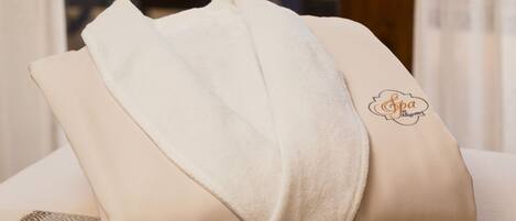 A neatly folded beige towel with a spa logo on a textured surface, likely a bed or a seating area, with a view of a dining table and chairs through a glass partition.