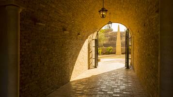 An arched brick corridor with a patterned floor, leading to an open area with a view of a distant structure.