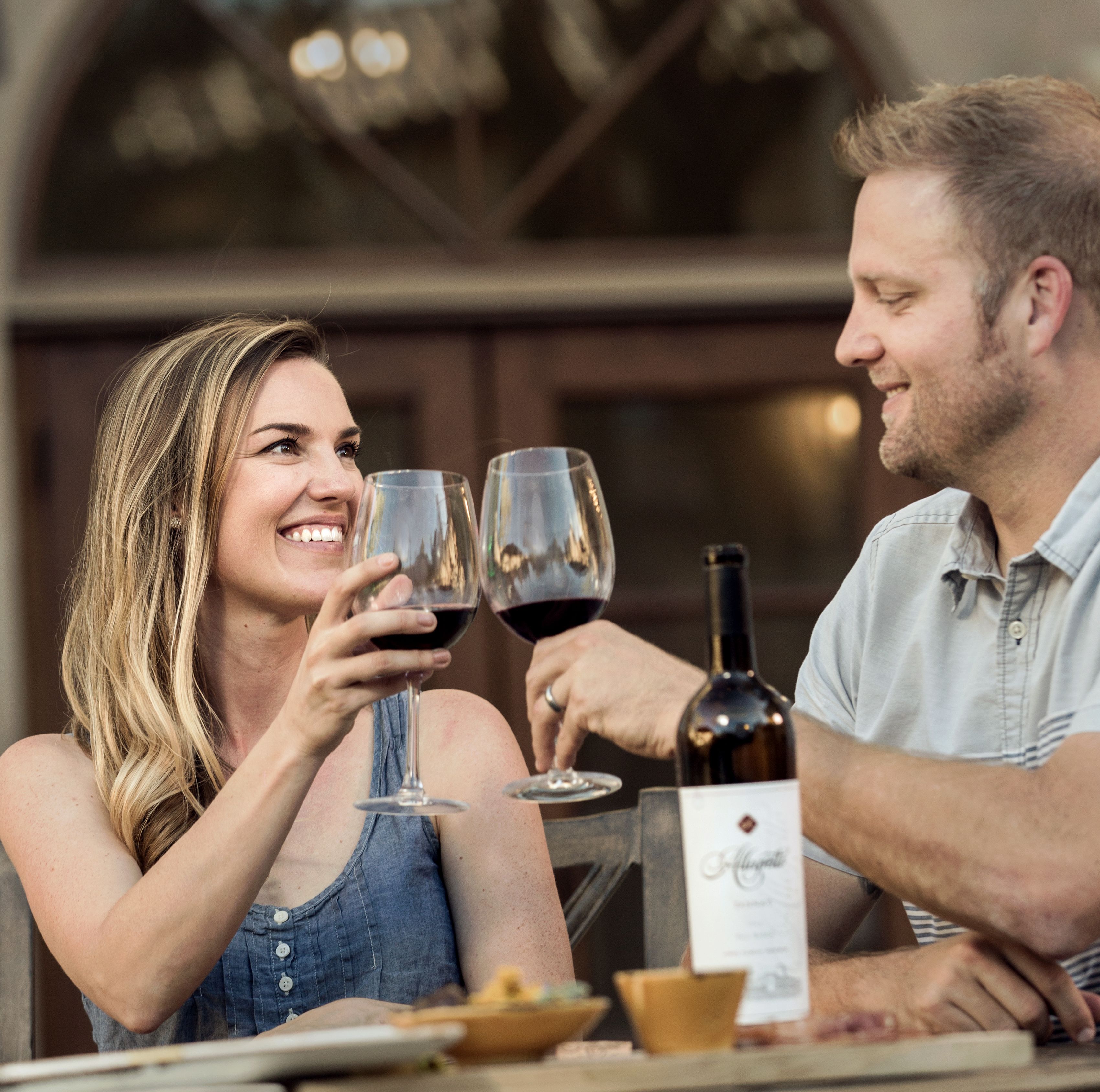 A couple sitting at a table with wine glasses, a bottle of wine, and a menu.