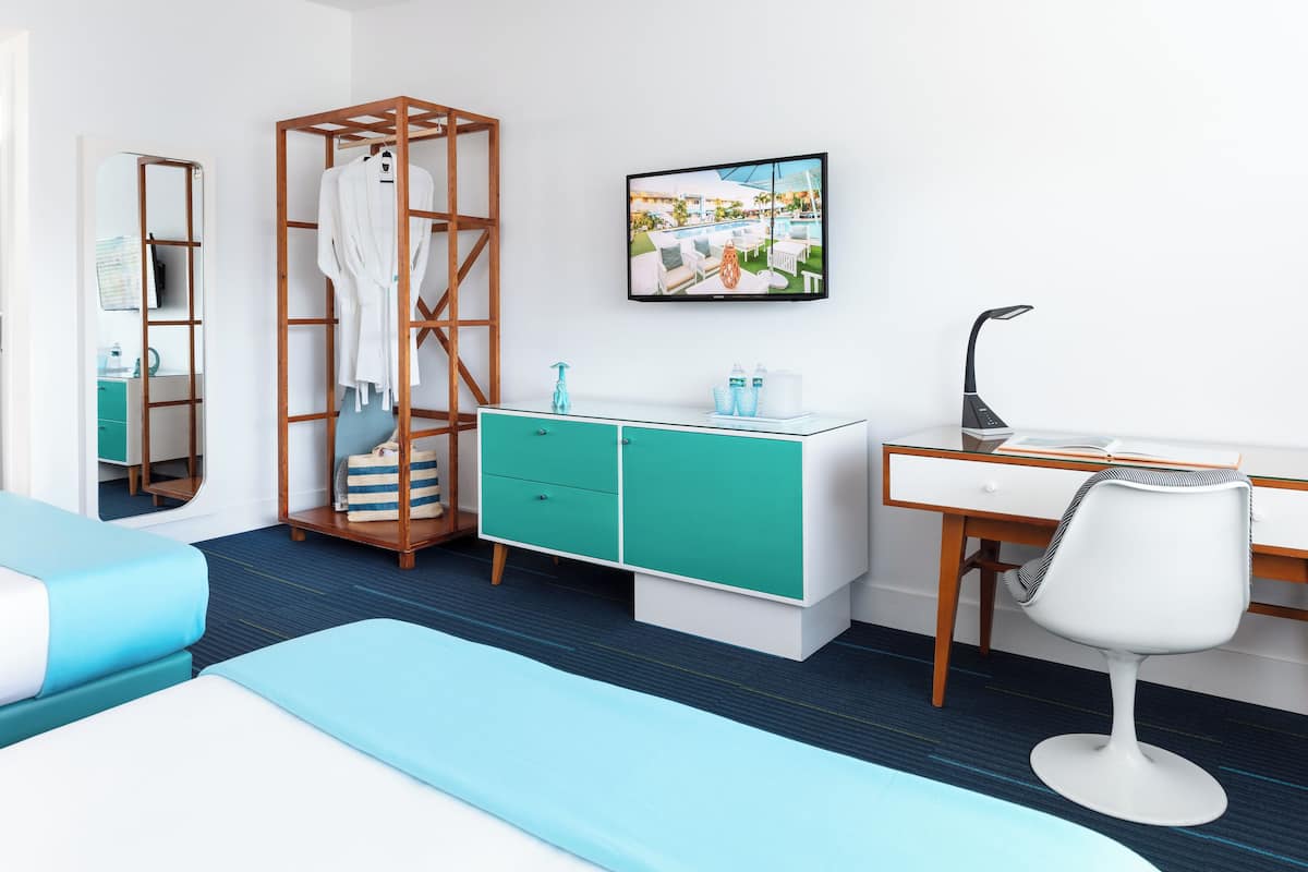 A modern hotel room with a bed, a desk with a chair, a wardrobe, and a bathroom visible through an open door.