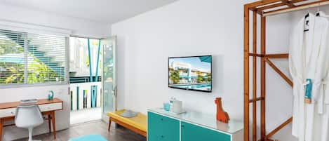 Una habitación de hotel moderna con cama, escritorio, televisor, un perchero de madera y un baño con toallero.
