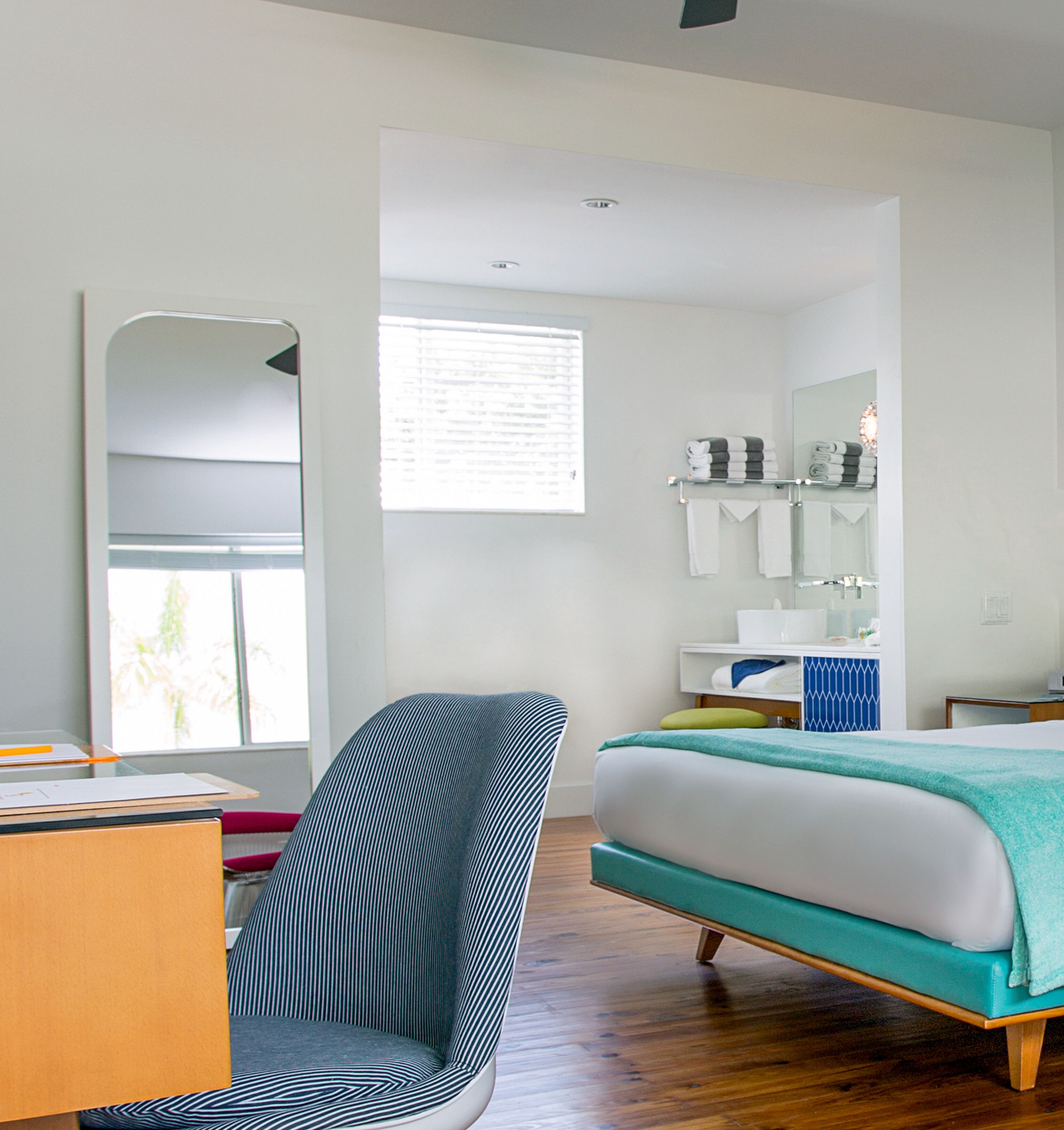 A modern bedroom with a bed, a chair, a desk, and a mirror.