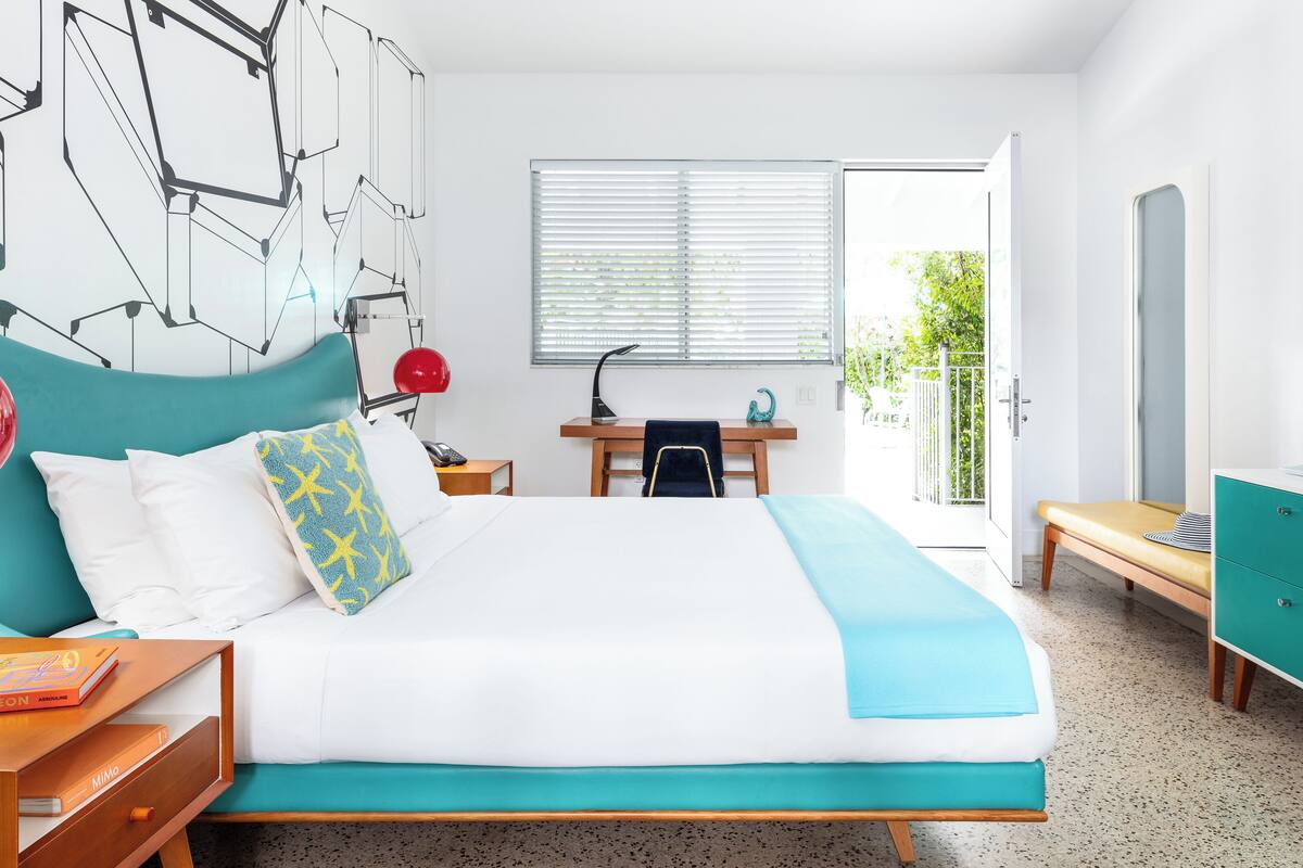 A modern hotel room with a bed, a desk, a chair, a wardrobe, and a balcony with a view.