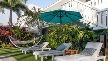 Un espace aménagé au bord de la piscine, avec des chaises longues blanches, un hamac et un grand parasol.