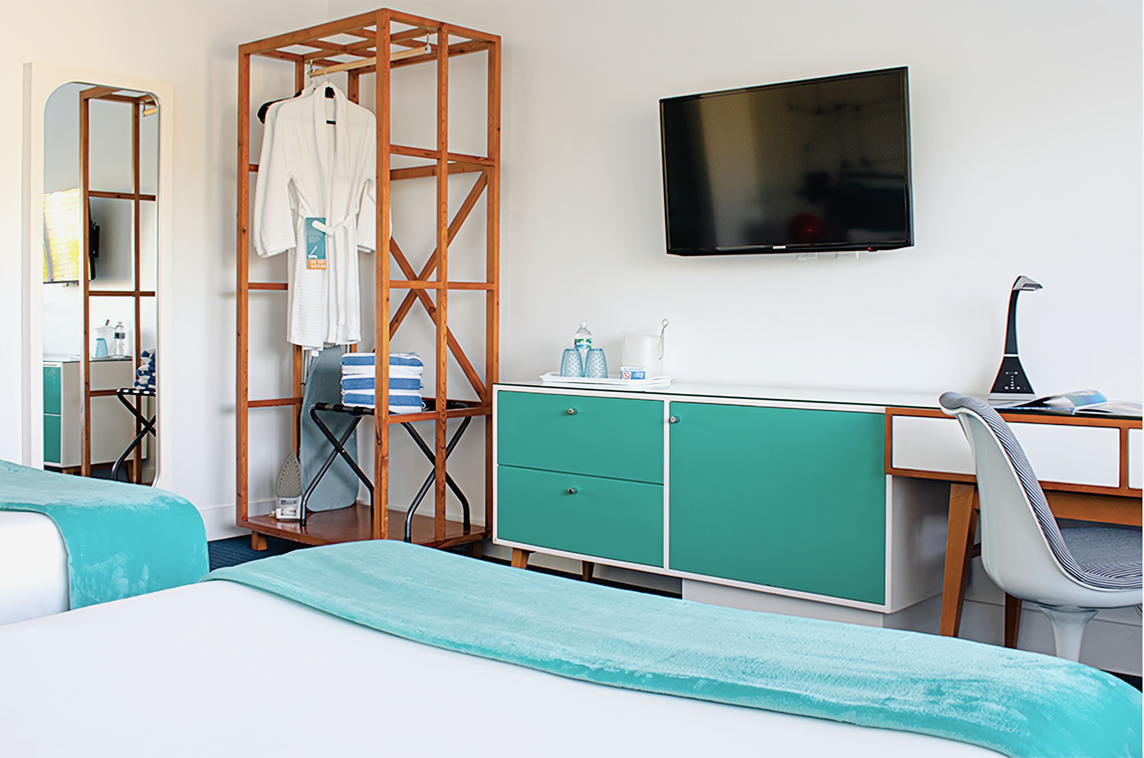 A hotel room with a bed, a desk with a computer, a TV, a wardrobe, and a mirror.