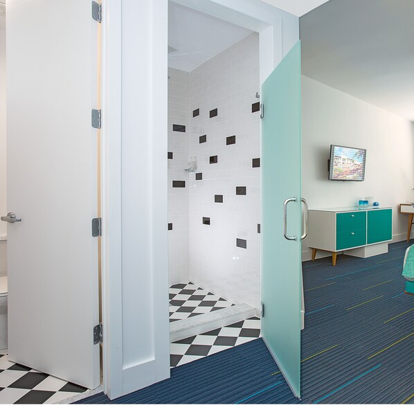 A hotel room with a checkered floor, a shower with white and black tiles, a teal cabinet, and a television on the wall. - The Vagabond Hotel Miami (Miami)