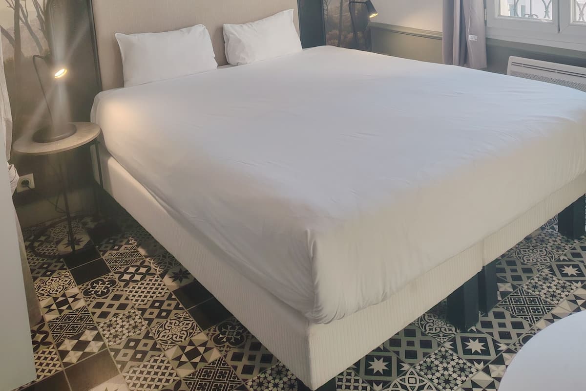 Een slaapkamer met een groot bed, een nachtkastje met een lamp, een muurschildering en een raam met gordijnen.