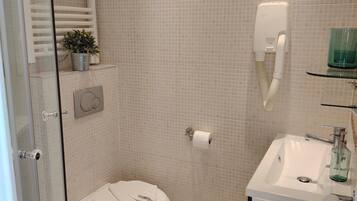 Une salle de bain comprenant des toilettes, une douche à parois de verre, un lavabo avec un miroir et un porte-serviettes.