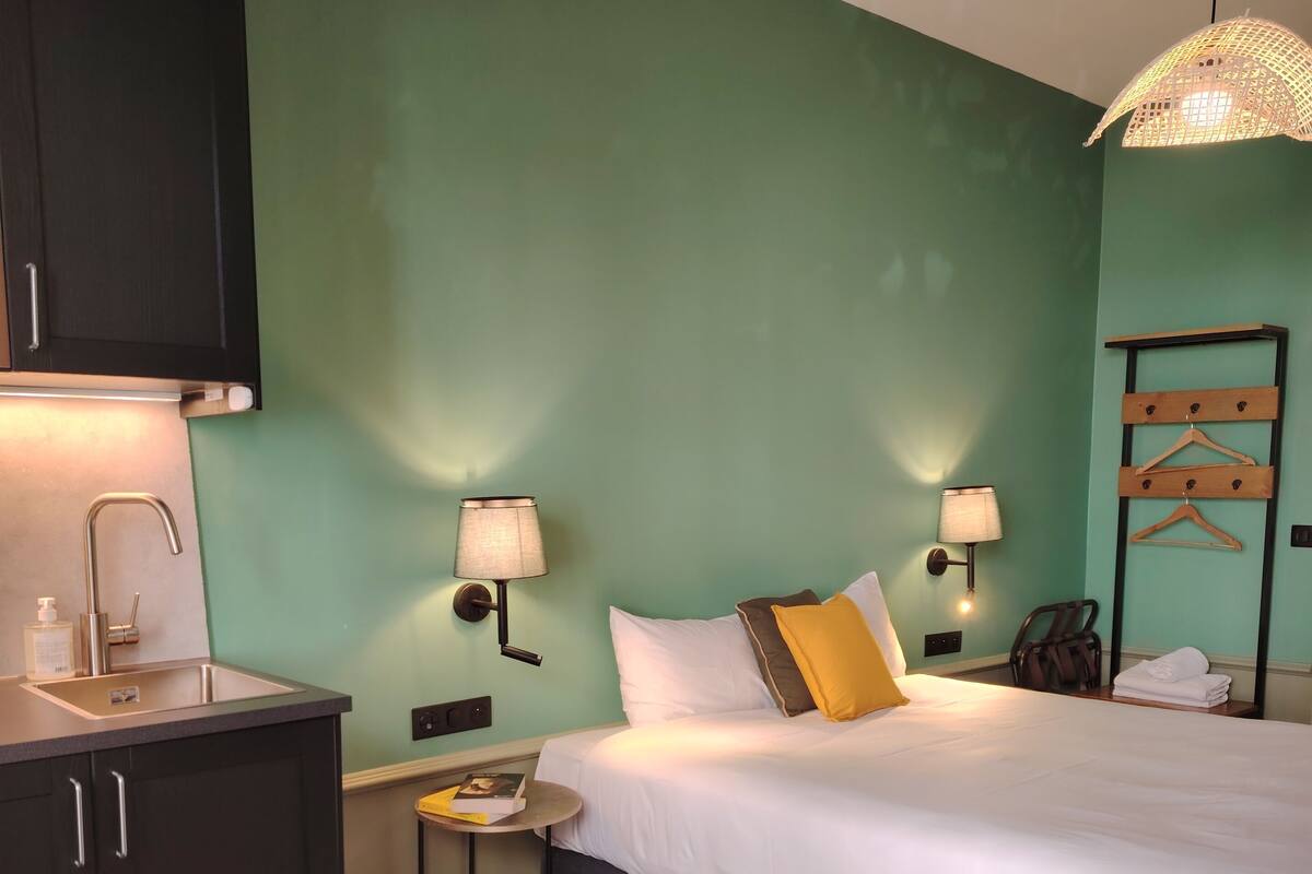 Een hotelkamer met een bed, nachtkastje, lamp en een klein rond tafeltje met een boek.