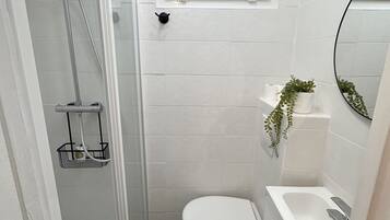 Un baño pequeño con ducha, inodoro y lavamanos.