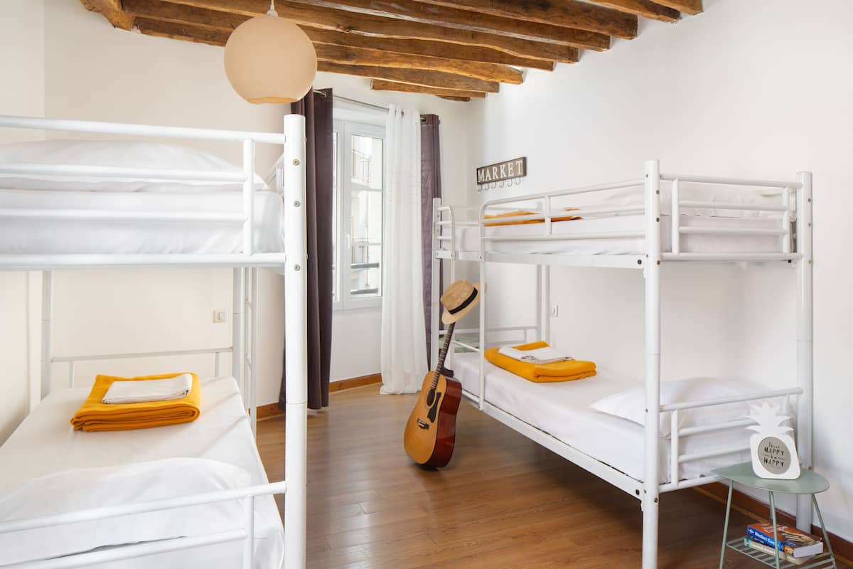 Een studentenkamer met stapelbedden, een gitaar en een klein tafeltje met een boek.