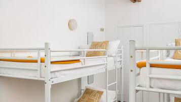 A dormitory room with bunk beds, wooden beams, white walls, and a skylight.