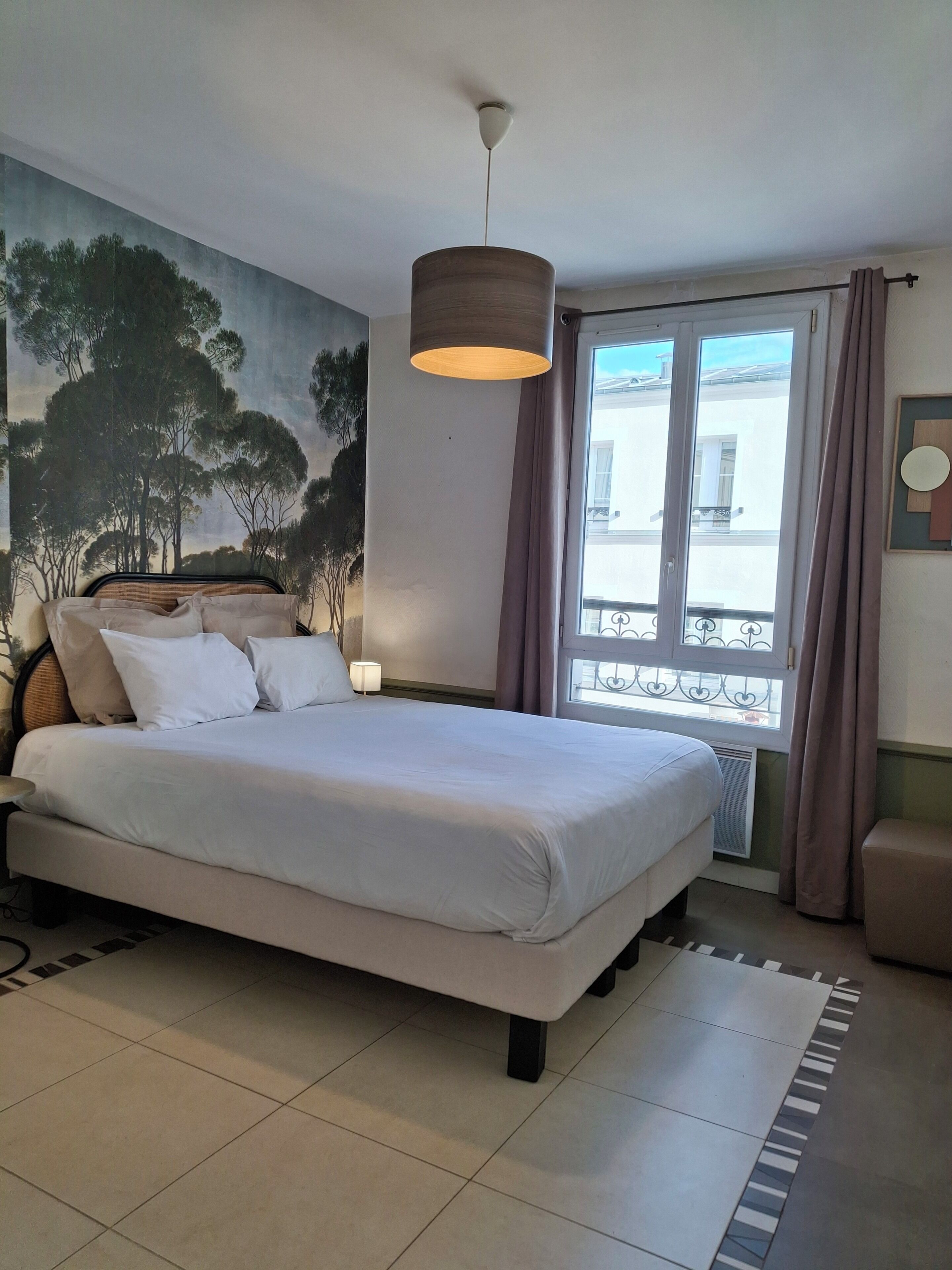 Une chambre à coucher avec un lit, une lampe suspendue, une fenêtre avec des rideaux et une fresque murale.