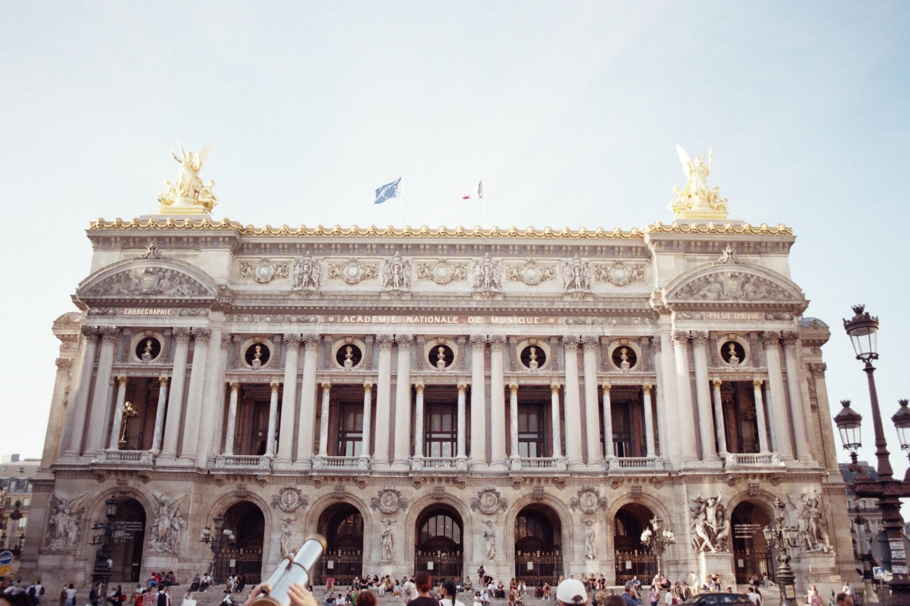 A large, ornate building with classical architecture, featuring multiple statues and columns.