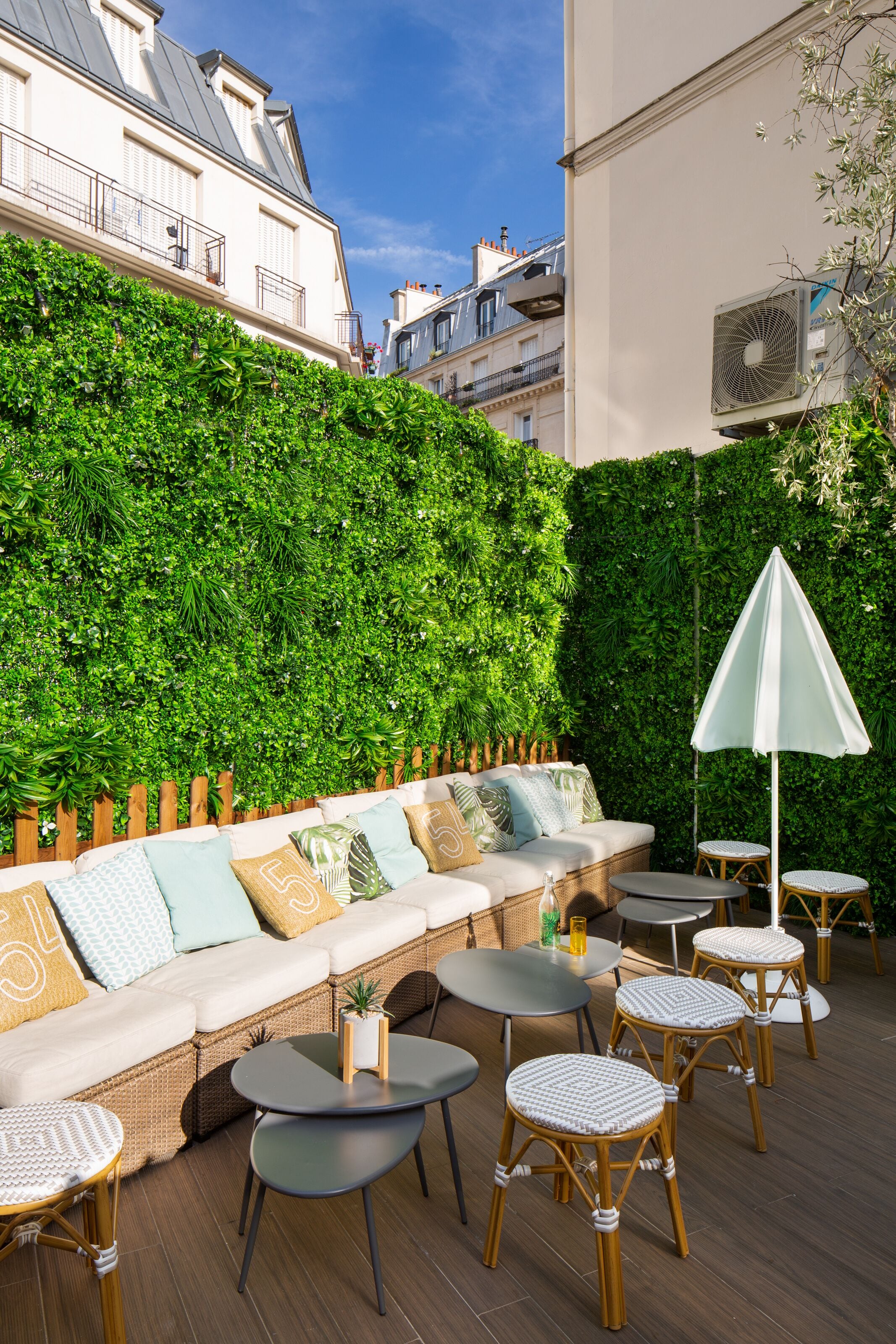 Een terras met een bank, stoelen en tafels, omgeven door een weelderige groene haag.