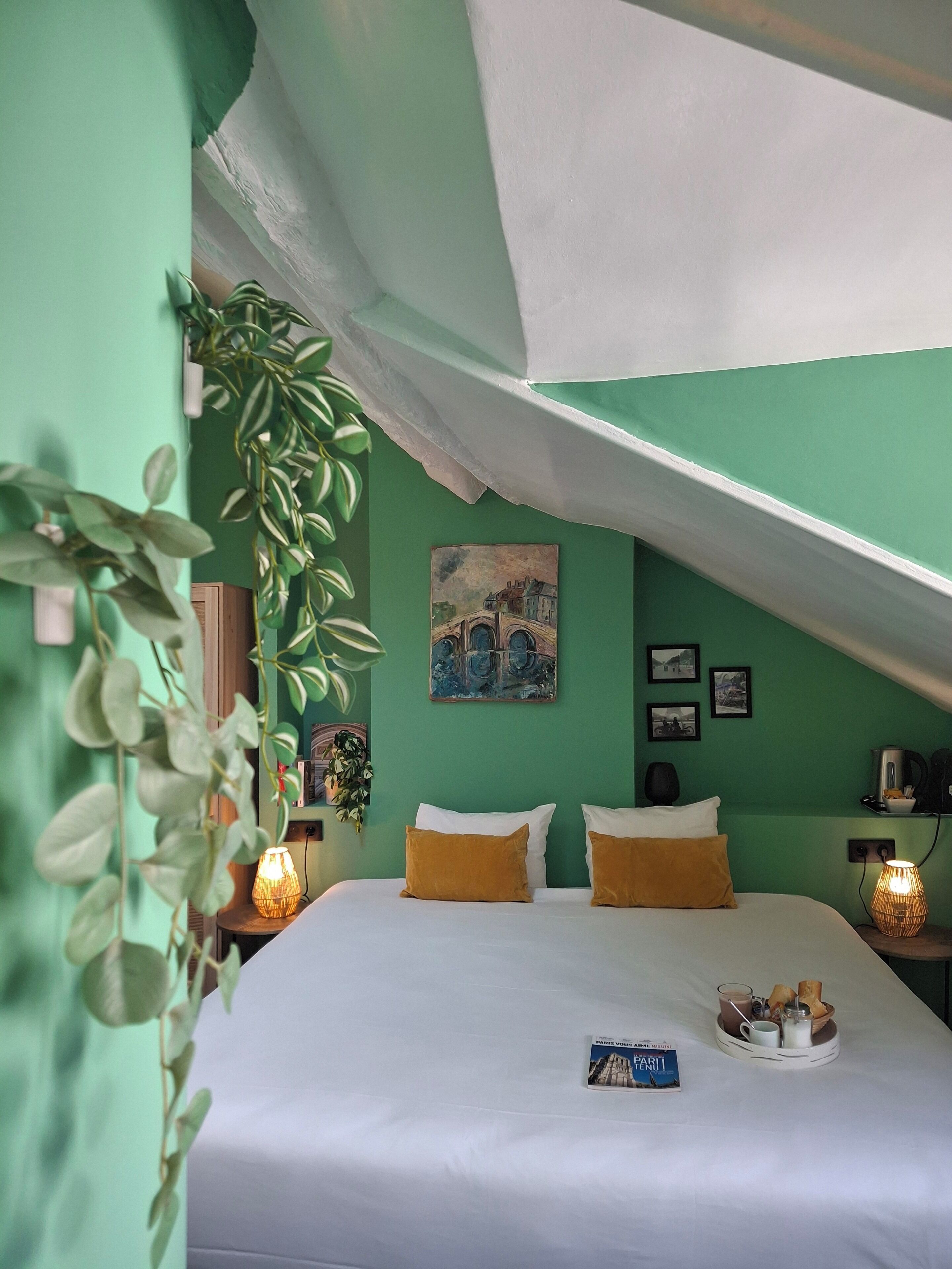 Une chambre avec un lit, des murs verts, un tableau et un plateau contenant des éléments pour le petit-déjeuner.