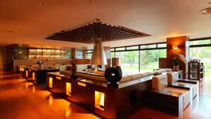 A modern hotel lobby with a bar area, seating arrangements, and large windows offering a view of the outdoors. - Lake Akan Tsuruga Wings (Kushiro)
