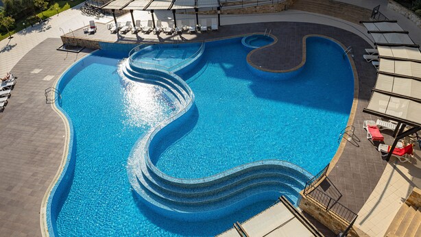 Una piscina con un diseño ondulado singular, rodeada de tumbonas y un área de estar cubierta.