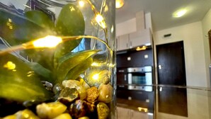 Primer plano de un florero de vidrio con una planta y guijarros, y electrodomésticos de cocina al fondo.