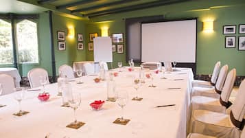 Une salle de conférence avec une longue table préparée pour une réunion, équipée de chaises, de verres à vin et d’un écran de projection.