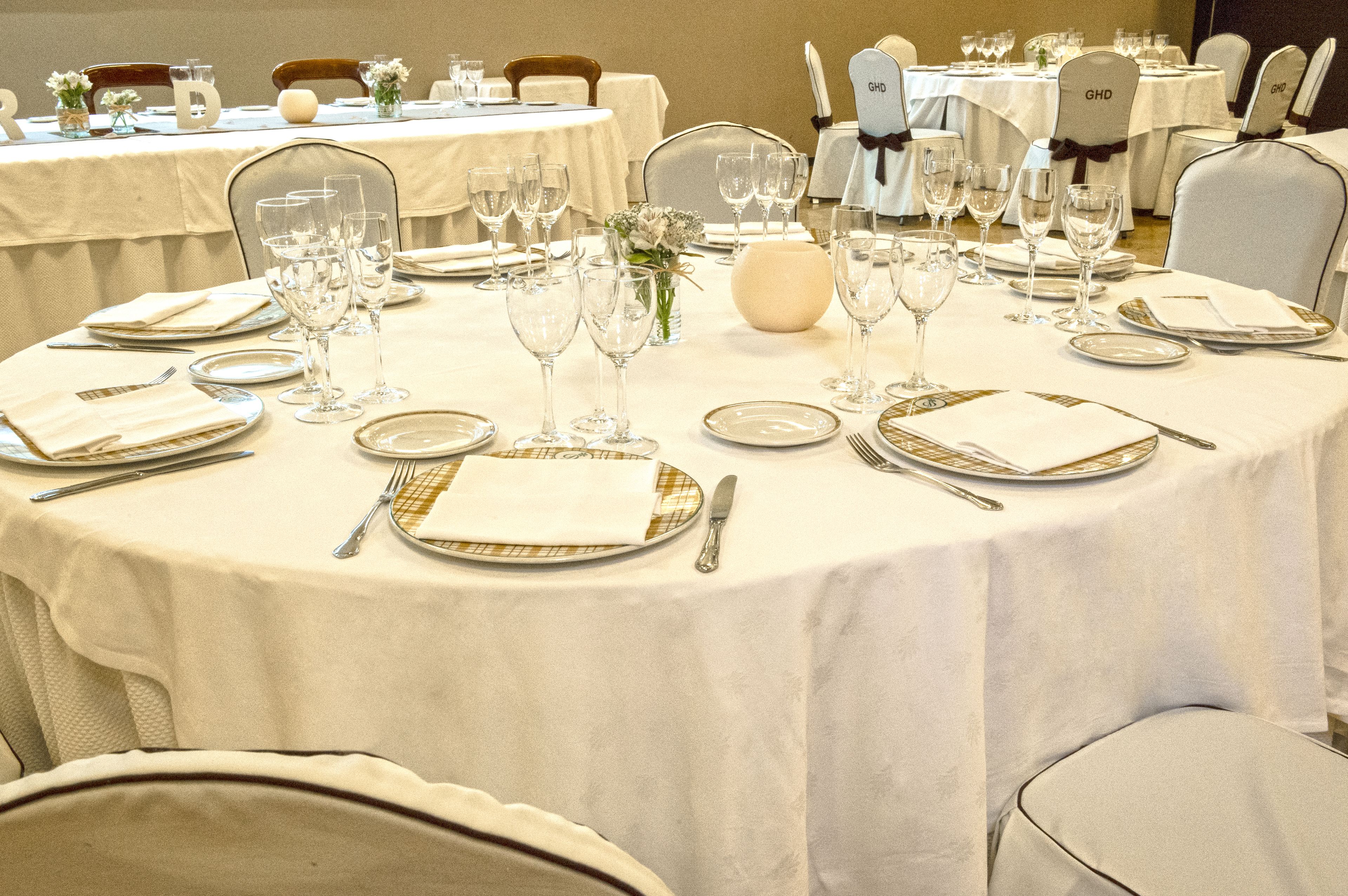 Een balzaal met ronde tafels gedekt voor een formeel evenement, elk voorzien van borden, bestek en wijnglazen.