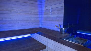 A sauna with wooden walls and a bench, a metal bucket, and a tray with items.