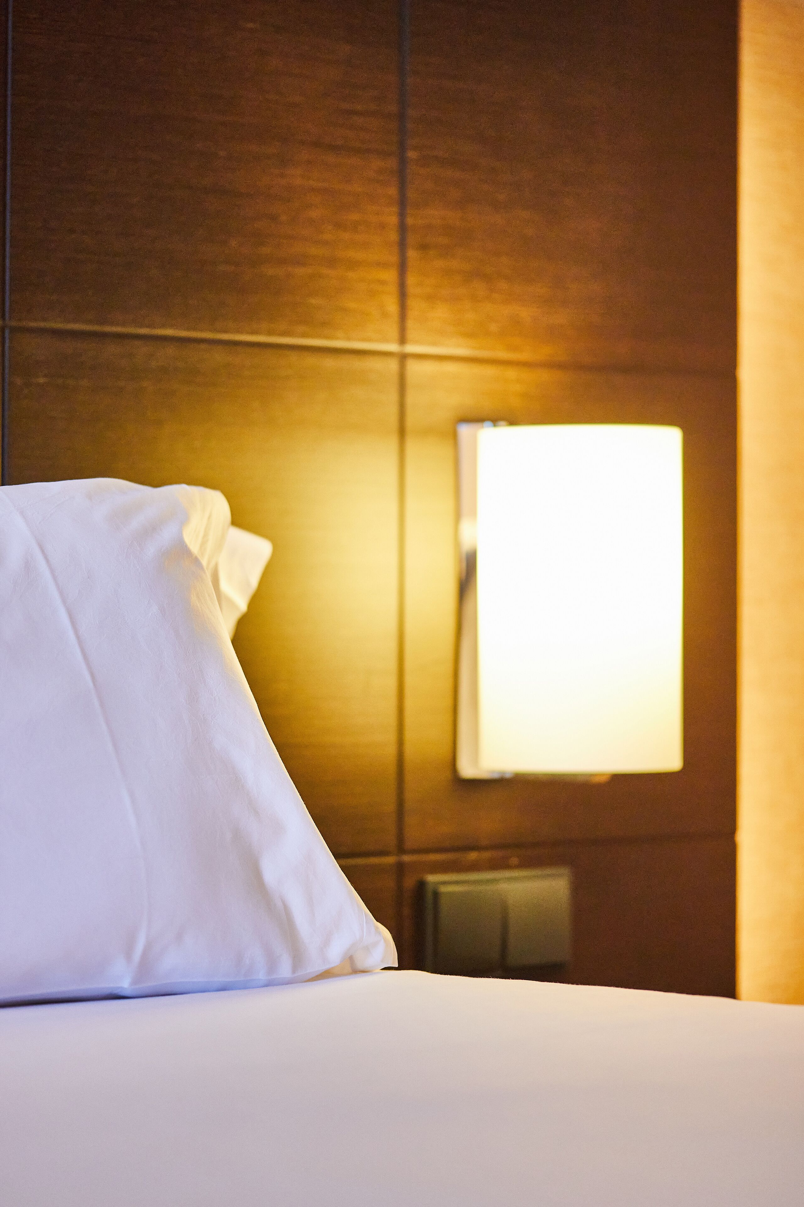 Une chambre d’hôtel avec un lit bien fait, une lampe fixée au mur et un thermostat.