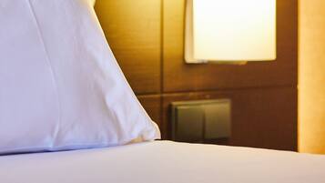Une chambre d’hôtel avec un lit bien fait, une lampe fixée au mur et un thermostat.