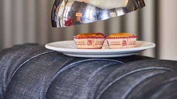 A hand holding a silver teapot over a plate with two cupcakes.