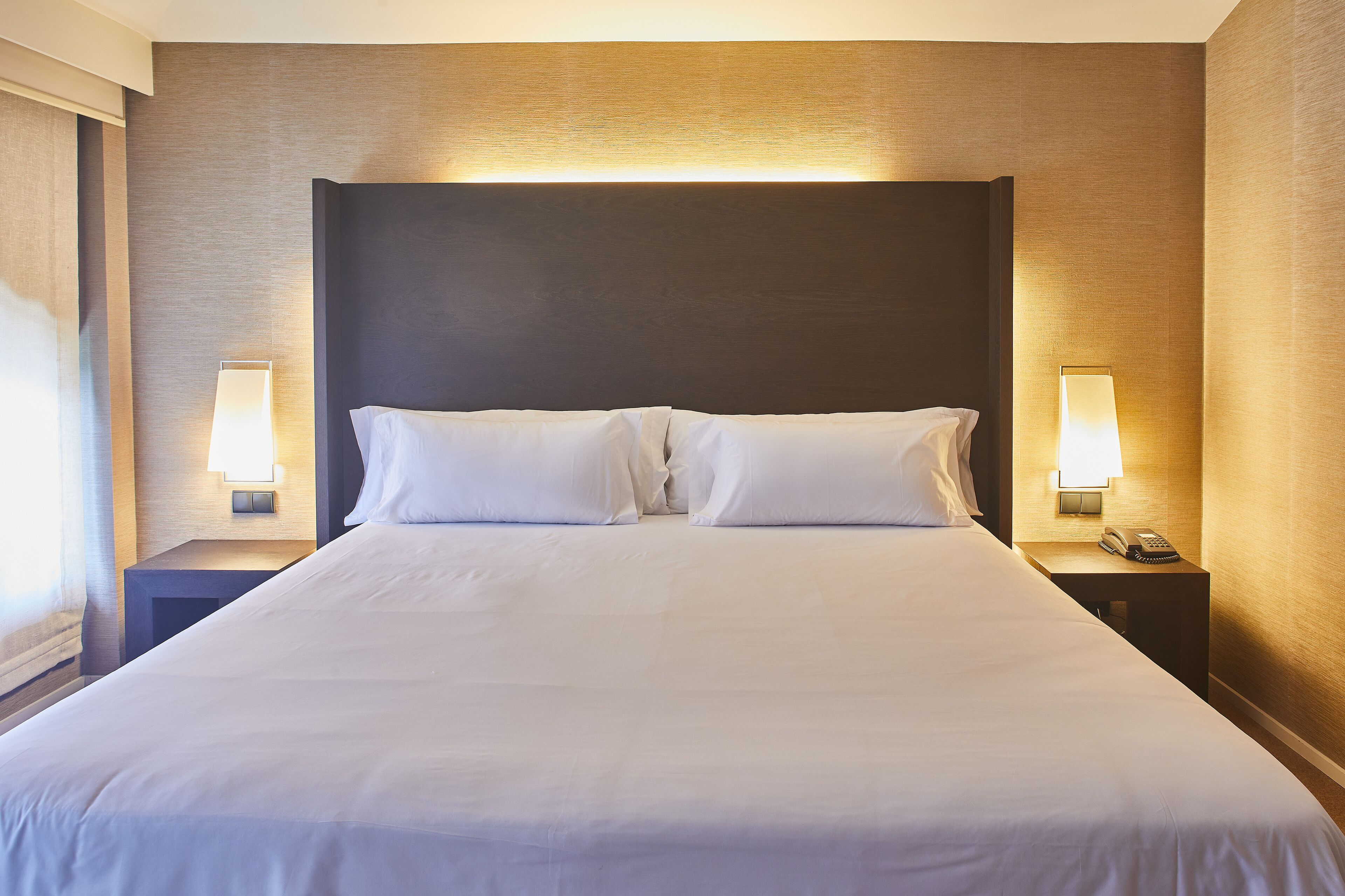 A neatly made bed with white linens and two bedside lamps on either side.