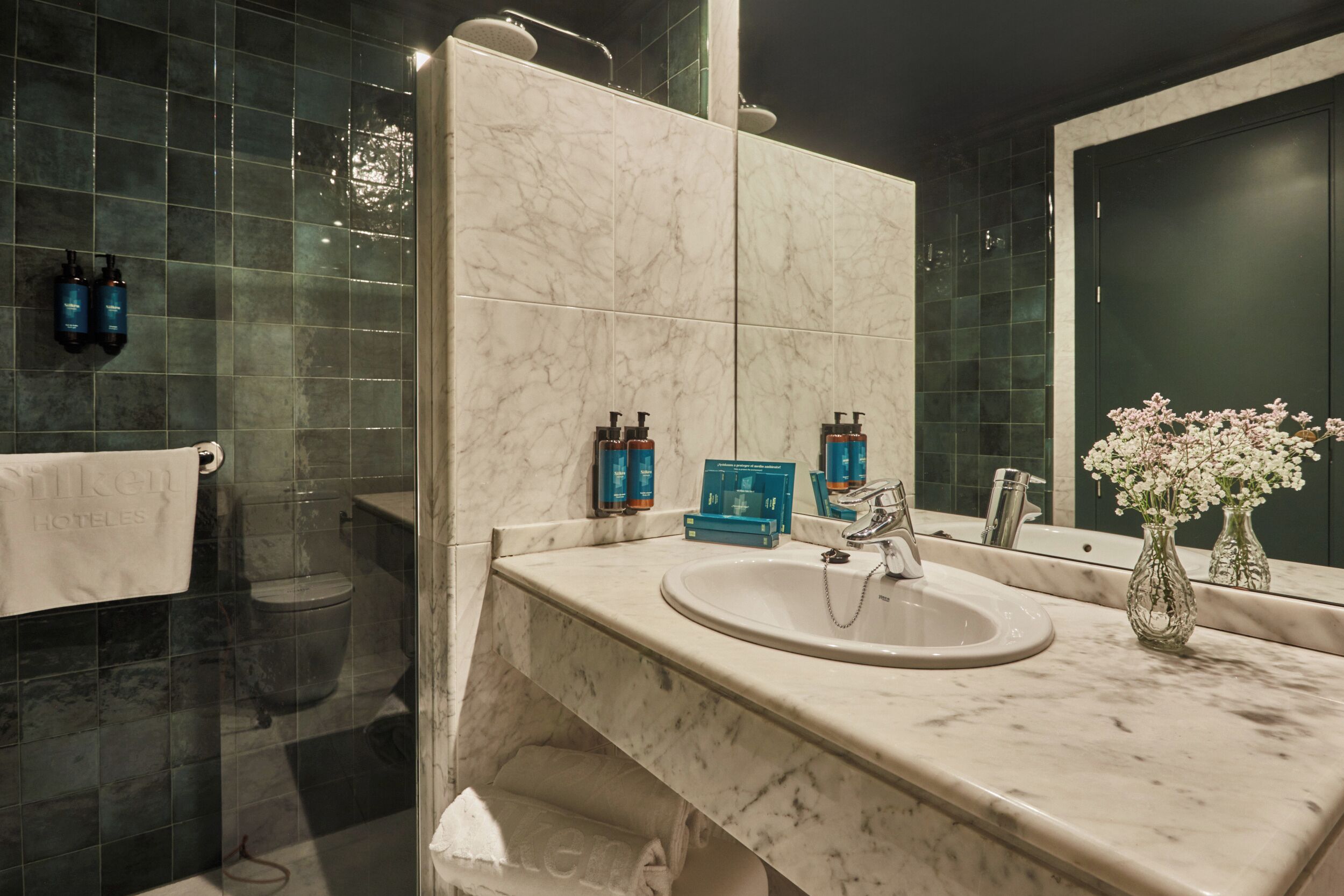 A bathroom with a marble sink, a large mirror, a towel rack, and a shower area.