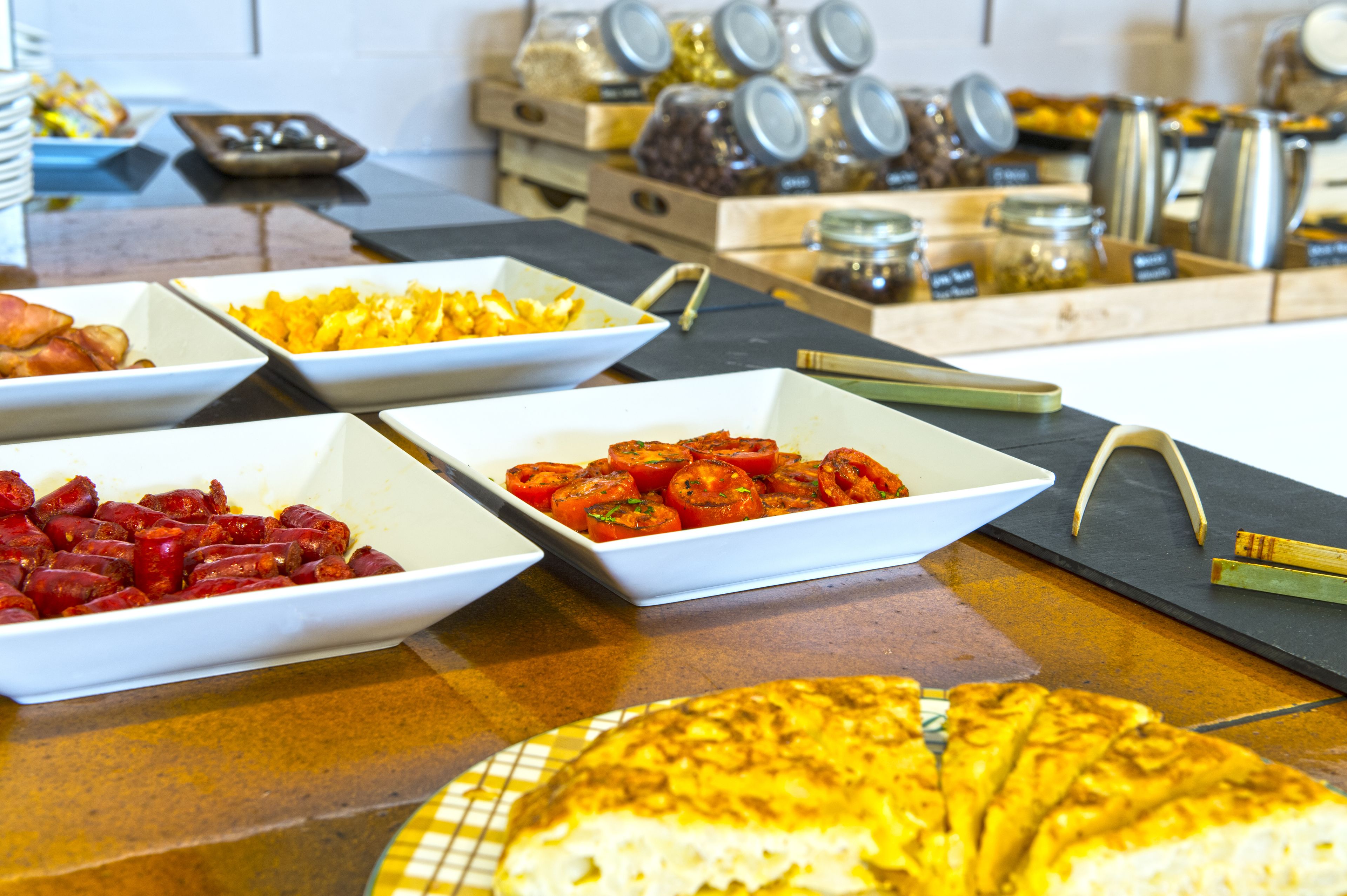 A buffet with various food items including a large pizza, bowls of sliced tomatoes, and other dishes.