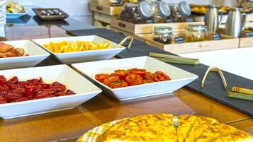 Een buffet met diverse gerechten, waaronder een grote pizza, schalen met gesneden tomaten en andere maaltijden.