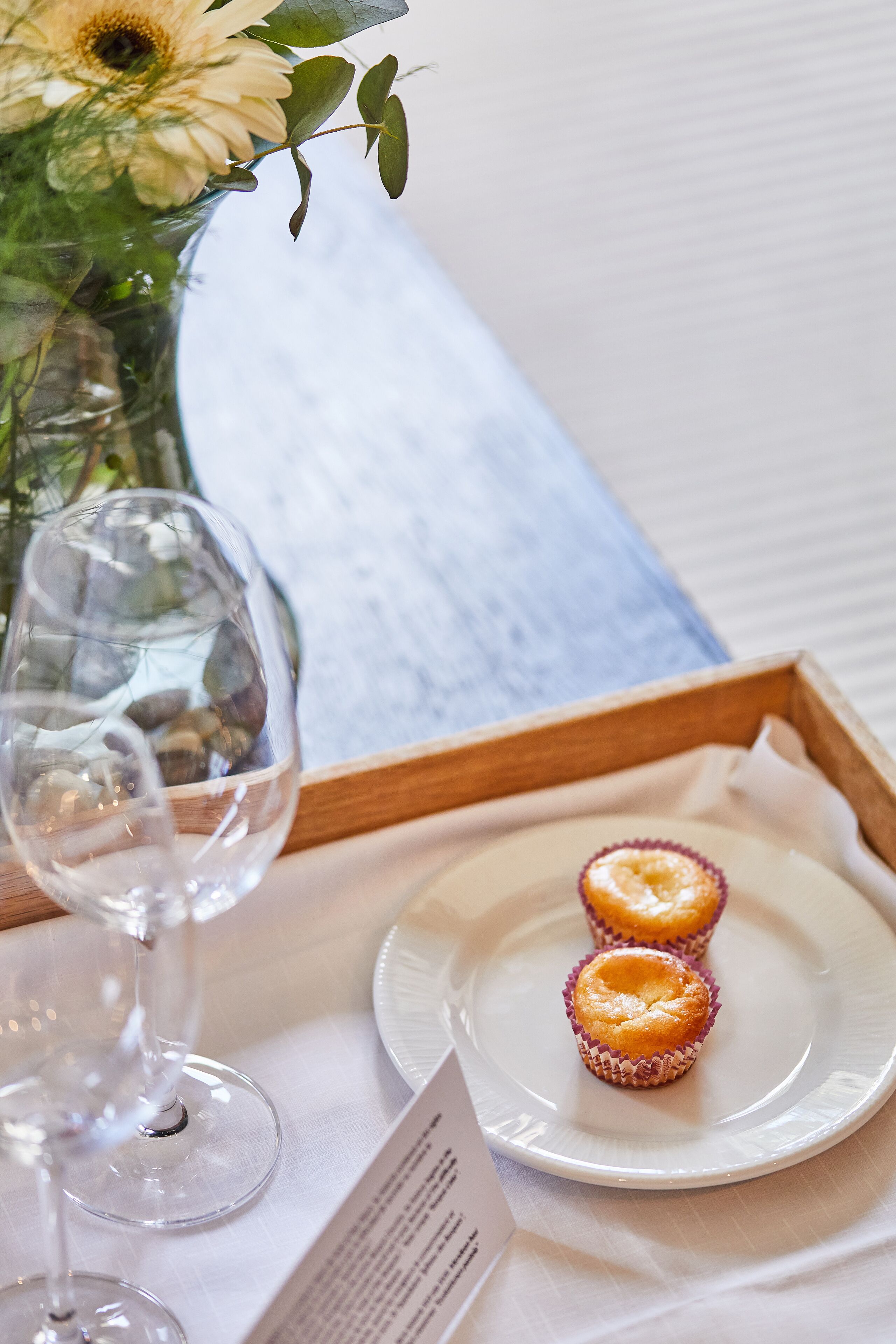 Une table sur laquelle se trouve une assiette blanche avec deux petits gâteaux, un verre à vin et un vase rempli de fleurs.