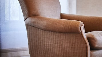 A brown armchair with wooden legs in a room with a plain wall and a window.