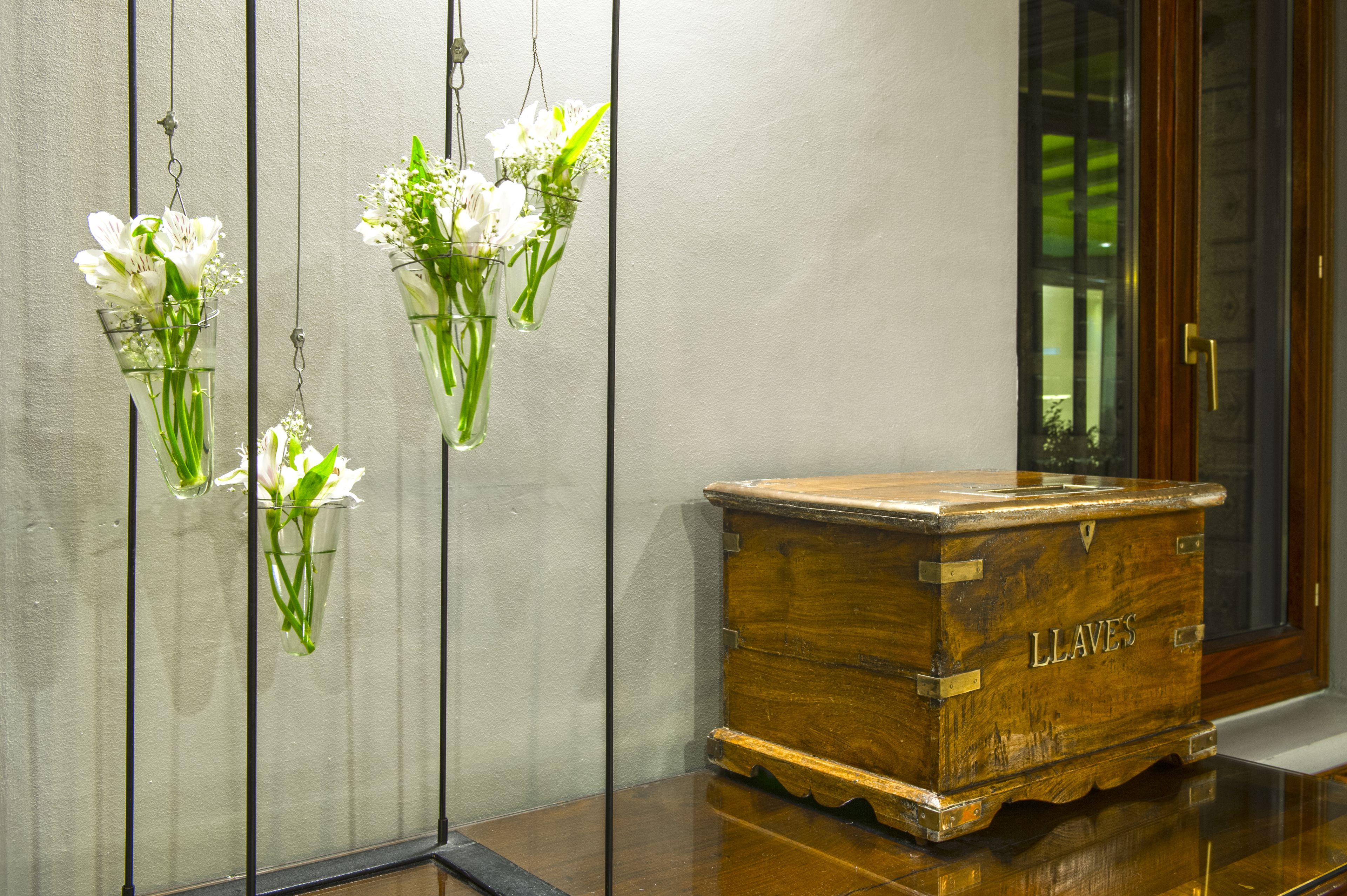 A wooden chest labeled "LLAVES" and three glass vases with white flowers against a wall.