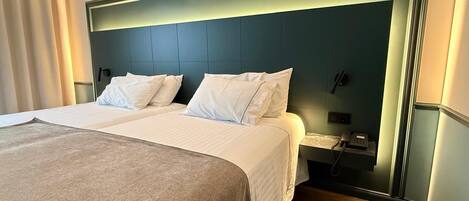 A hotel room with a large bed, a bedside table with a phone, and a headboard with built-in lighting.