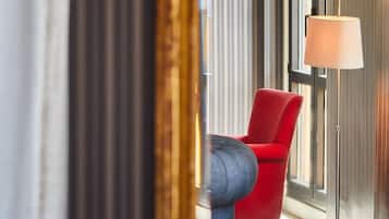 Una habitación de hotel con una silla roja, una lámpara de pie y un ventanal con cortinas.