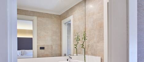 Une salle de bain moderne avec un grand miroir, un lavabo blanc et une petite plante.