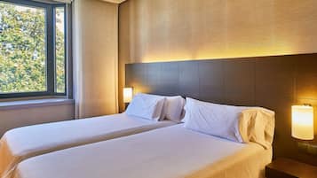 A hotel room with two beds, a large window, and a wall-mounted lamp.